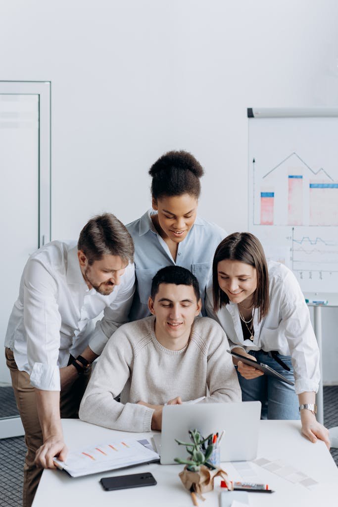 A diverse team of colleagues collaborating around a laptop in a modern office.
