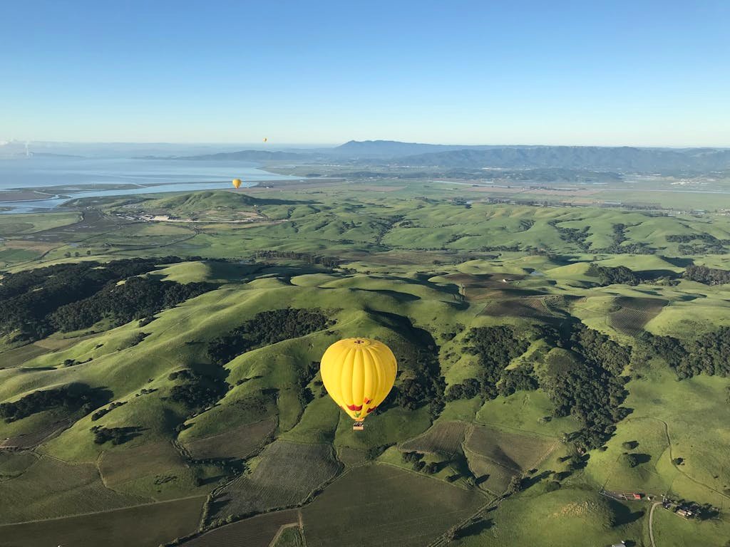 A tranquil view of hot air balloons floating above lush Californian hills under a clear blue sky.